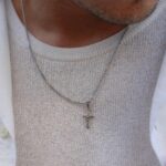 Close-up de homem a usar colar com corrente fina e cruz religiosa prateada
